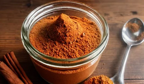 Piles of individual spices that make up homemade pumpkin pie spice rest on a leaf from a corn stalk. In the background is a sparkly yellow pumpkin and a sprig of greene ry. Everything sits on a picnic table. This is the designated pinterest pin.