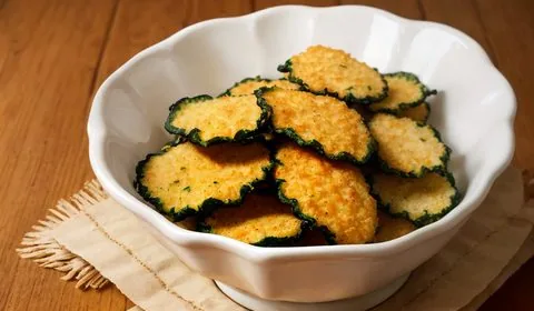 At the top, a bowl of lightly mixed eggs, a bowl of homemade bread crumbs, and a container of raw zucchini slices sit on a countertop. At the bottom, the finished breaded zucchini chips sit on an aluminum foil covered baking sheet. This is the designated pinterest pin.