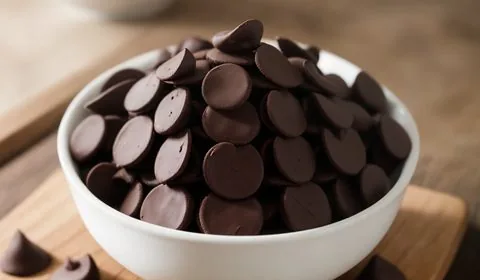 A large pile of homemade chocolate chips sit on a light colored wooden cutting board. This is the designated pinterest pin.