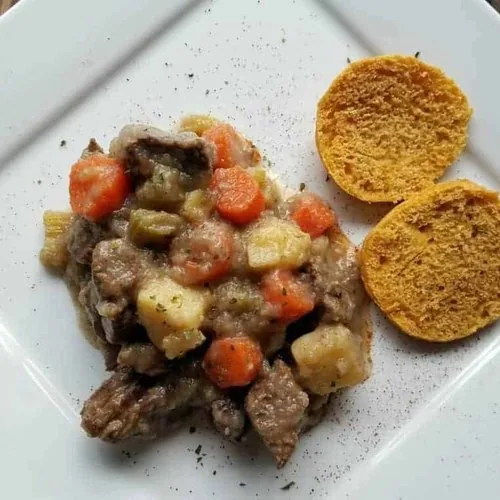 Stove top beef stew with a sweet potato biscuit on a white square plate.