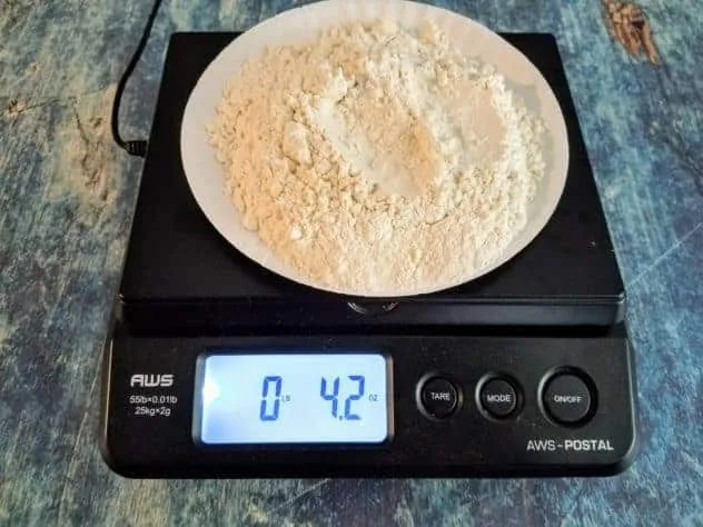 Blueberry Buttermilk Pancakes Process Step 1a A paper plate holding flour rests on top of a weighing scale on a blue background.