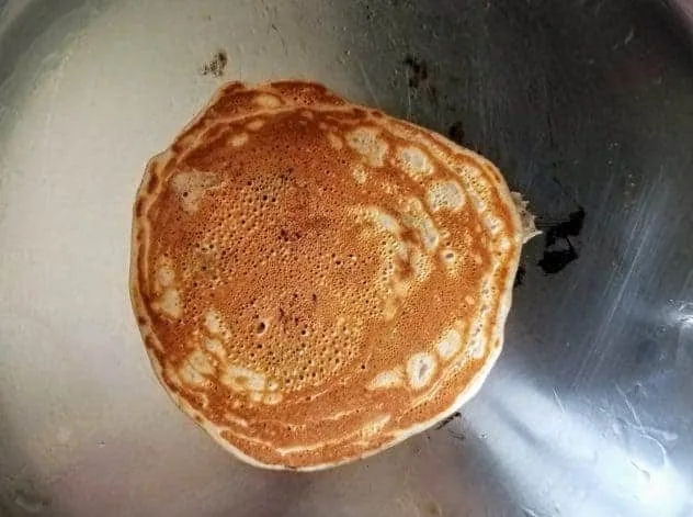 Blueberry Buttermilk Pancakes Process Step 4b A fully cooked lightly golden colored blueberry buttermilk pancake in a stainless steel pan.