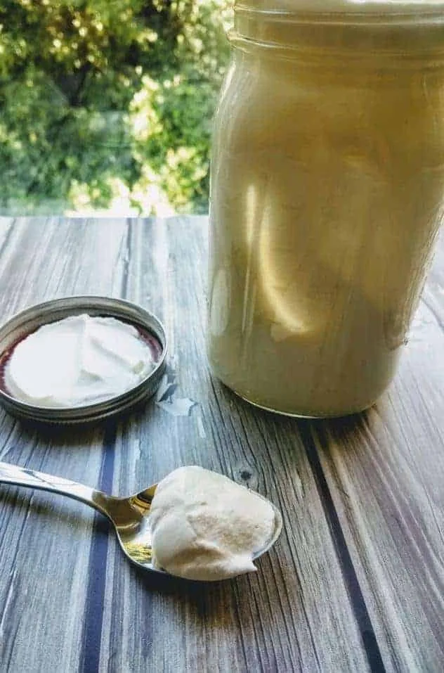 Whipped cream in a large mason jar on a gray wood plank background. A spoon with a scoop of whipped cream sits next to the jar.