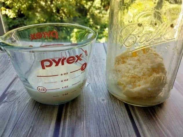 Buttermilk in a Pyrex measuring cup and homemade butter in a large mason jar. Both sit on a gray wood plank background.