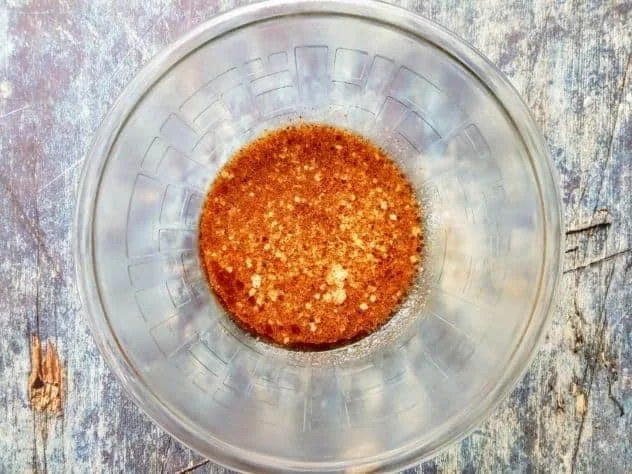 Chocolate Chip Oatmeal Pulp Cookies Process Step 2 Baking powder, ground cinnamon, Kosher salt, light brown sugar, and quick oats mixed into the wet ingredients in a large glass bowl sitting on a blue background.