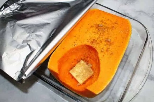 Baked Butternut Squash Process Step 6 A piece of aluminum foil is being loosely placed over the pan before putting the butternut squash into the oven to bake.