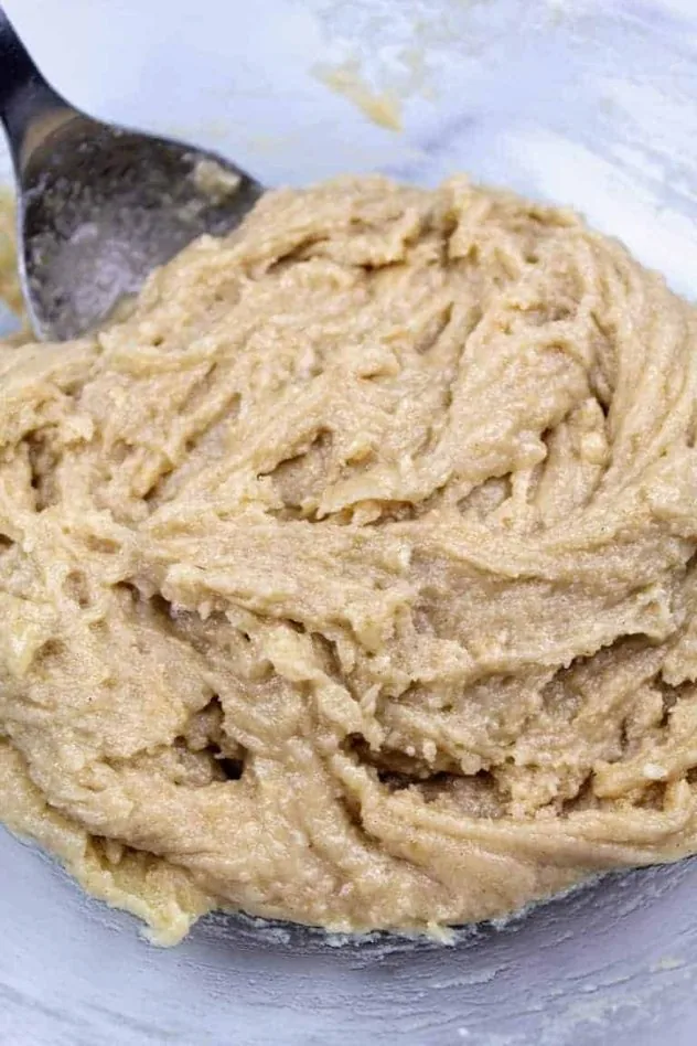 Dairy Free Chocolate Chip Cookies Process Step 2 Dough after mixing in two cups of gluten-free flour. Everything sits in a large glass bowl with a stainless steel mixing spoon.