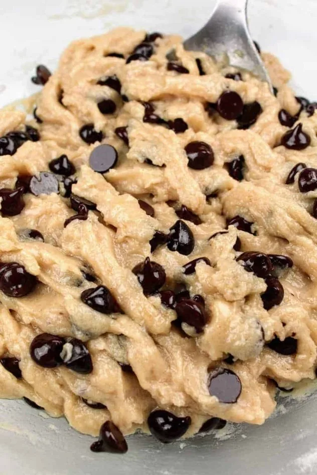 Dairy Free Chocolate Chip Cookies Process Step 3 The final cookie dough after folding in the chocolate chips. Everything sits in a large glass bowl with a stainless steel mixing spoon.
