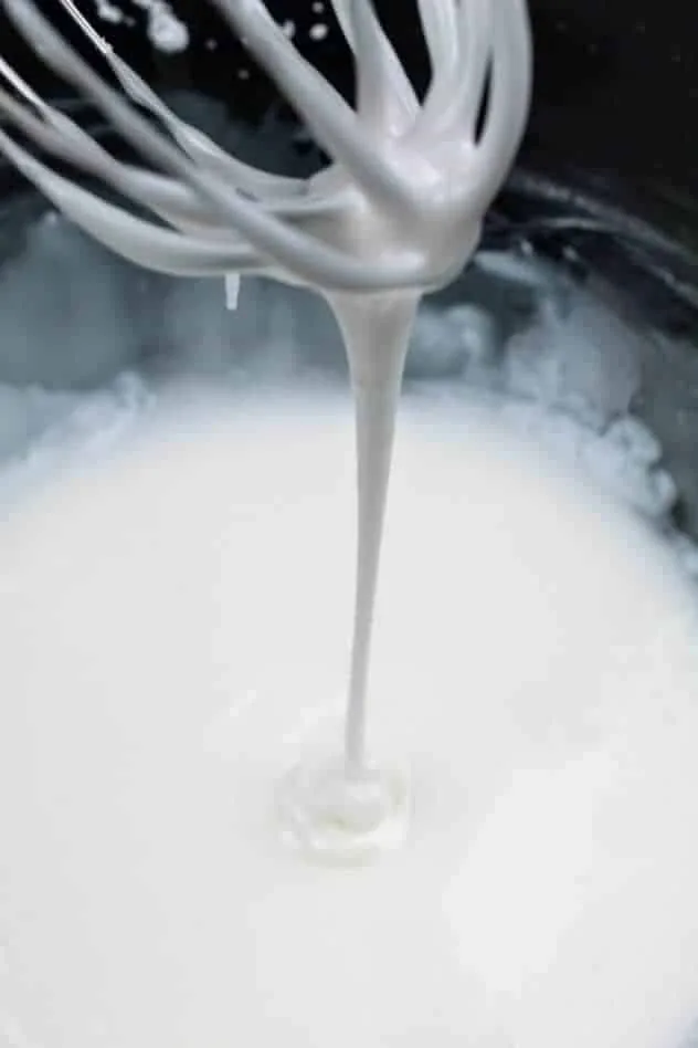 Gluten-Free Ricotta Cookies Process Step 5 Confectioner's sugar glaze drizzling from a wire whisk into a large glass bowl filled with the rest of the glaze.