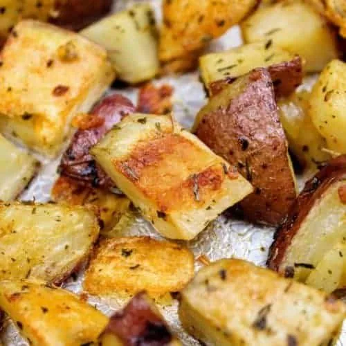 Roasted herb red potatoes sitting on a textured aluminum baking sheet. The potatoes are golden brown and wrinkled from roasting in the oven. This is the horizontal image.