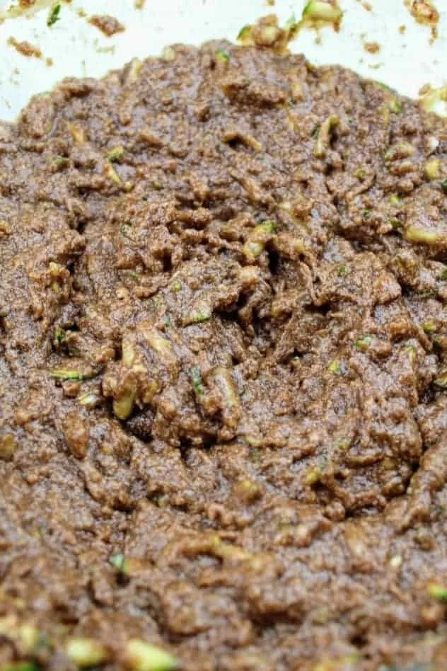 A mixture of grated zucchini, light brown sugar, coconut oil, vegan butter, applesauce, vanilla extract, cinnamon, baking soda, cocoa powder, and Kosher salt in a large glass mixing bowl.