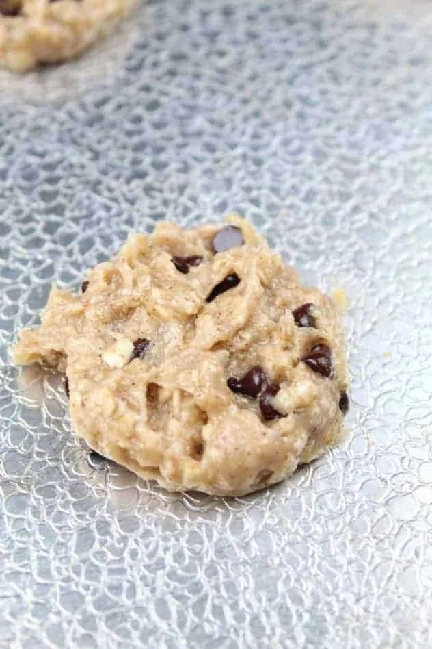 A single, flattened, unbaked cookie on a textured aluminum baking sheet.