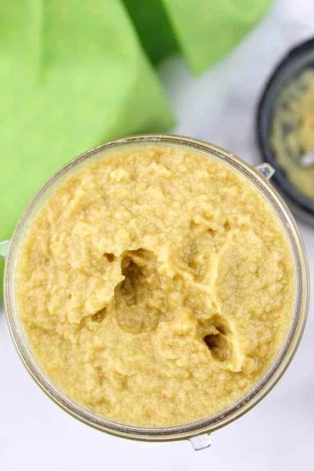 In the center is the final vegan key lime hummus all blended together in the blending container. In the upper left is a lime green tea towel and in the upper right is the bottom part of the blending container with the blades.