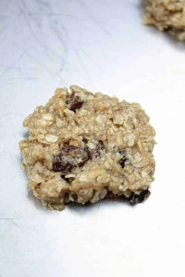 A single vegan oatmeal raisin cookie sits on a greased aluminum baking sheet prior to baking.