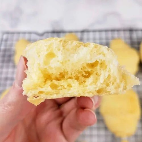 A close up of the inside of a homemade crescent roll. In the background are the rest of the rolls sitting on a wire cooling rack. This is the vertical image.